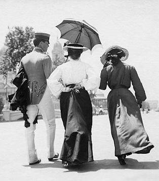 A group of three well-dressed people in the early 20th century, walking in a public park in St. Louis